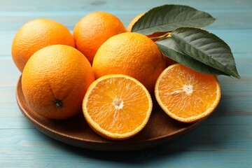 Fresh oranges and leaves on light blue wooden table, closeup