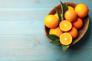 Fresh oranges and leaves in wicker basket on light blue wooden table, top view. Space for text