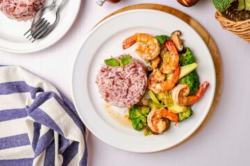 Stir fried broccoli with shrimp,shitake mushroom and riceberry in a white ceramic plate witn spoon and fork on white table background, clean food concept