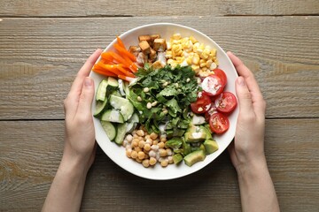 Woman with different healthy vegetarian food at wooden table, top view