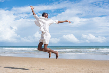 A young carefree woman jumping on sand beach,african female enjoying a summer vacation day in sea...