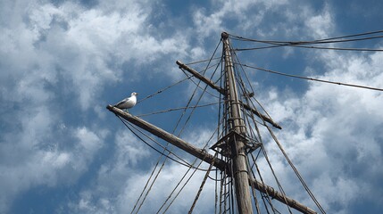 Ship mast with a bird perched on it against a cloudy blue sky.