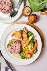 Stir fried broccoli with shrimp,shitake mushroom and riceberry in a white ceramic plate witn spoon and fork on white table background, clean food concept