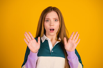 Cute woman expressing surprise with hands raised against yellow background, wearing casual pullover