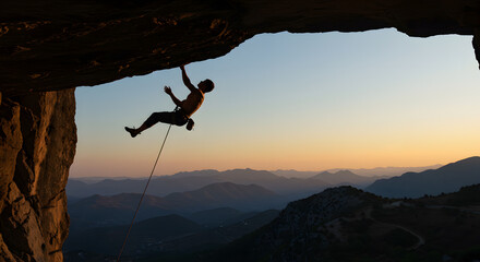 Athletic man climbs an overhanging rock with rope, lead climbing. silhouette of a rock climber on a mountain background. outdoor sports and recreation