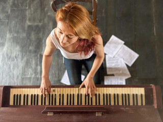 Ginger-haired woman, 30s, playing an old  piano at home. High-angle view of her  with sheet music...