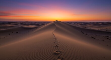 Footprints on a sand dune under a colorful sunset sky in a desert landscape with rolling sand dunes