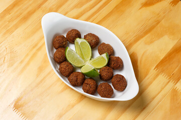 Delicious portion of fried kibbeh balls with fresh lime wedges, served in a white ceramic bowl on a wooden table.
