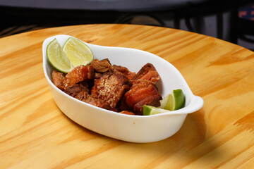 Pork rinds (torresmo), typical Brazilian food with fresh lime wedges, served in a white ceramic bowl on a wooden table.