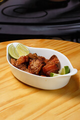 Pork rinds (torresmo), typical Brazilian food with fresh lime wedges, served in a white ceramic bowl on a wooden table.