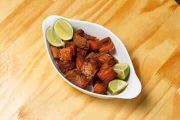 Pork rinds (torresmo), typical Brazilian food with fresh lime wedges, served in a white ceramic bowl on a wooden table.