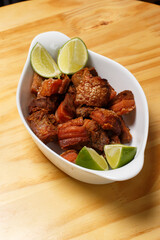 Pork rinds (torresmo), typical Brazilian food with fresh lime wedges, served in a white ceramic bowl on a wooden table.