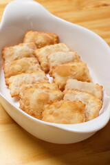 Delicious portion of fried pastries served in a white ceramic bowl on a wooden table.