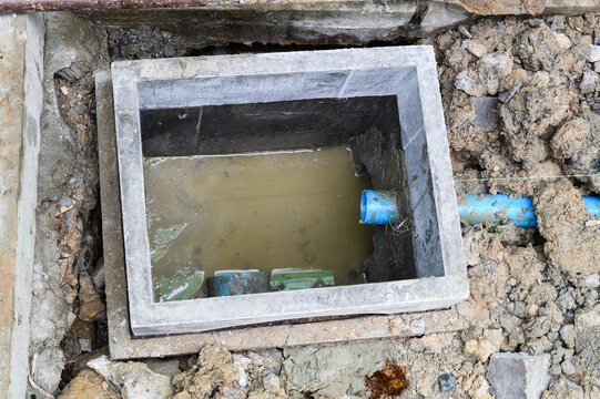 Problematic open concrete drain pit with dirty water during messy house renovation. damaged septic system or plumbing awaiting repair underground with blue PVC pipe