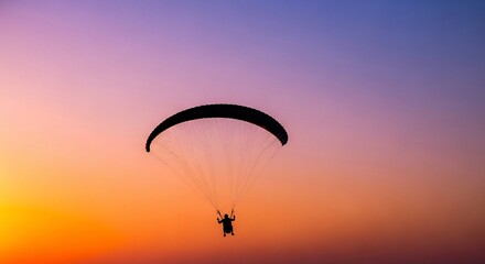 Silhouette of a person paragliding against a vibrant, colorful sunset sky.