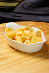 Delicious portion of fried manioc, or cassava, served in a white ceramic bowl on a wooden table.