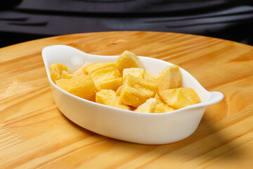 Delicious portion of fried manioc, or cassava, served in a white ceramic bowl on a wooden table.