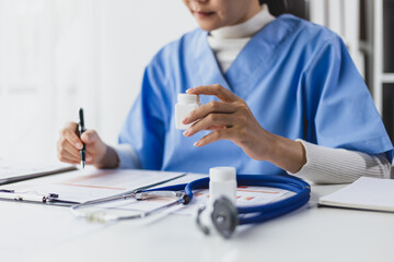 Female doctor reading and writing prescriptions in hospital office. The doctor is calculating the...