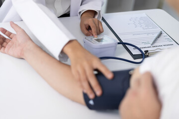 Female doctor measuring blood pressure of patient in hospital room. Doctor using sphygmomanometer...