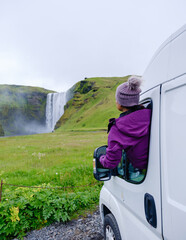 A traveler enjoys the breathtaking view of Skogafoss waterfall in Iceland, peering out from a...
