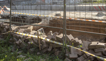 Excavated section of street during repair of underground heating system, surrounded by temporary fence. Pile of construction debris in the foreground