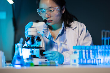 Scientist using microscope analyzing samples in laboratory at night, conducting scientific research.