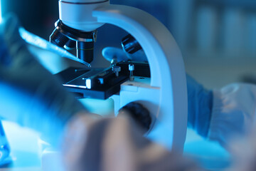 Scientist placing sample on microscope slide in laboratory, conducting scientific research. Scientists are dropping chemicals onto a slide on a microscope.