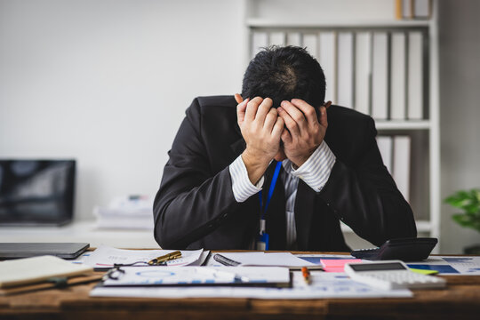 Stressed businessman sitting at his desk, his desperation and frustration, surrounded by documents and office supplies.