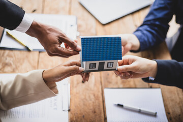 Real estate agents are holding a miniature house model during a meeting, property sales,...