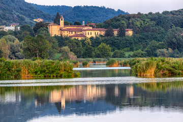 View of a serene lake reflecting the warm hues of an ancient building nestled among lush green trees, a tranquil escape into nature, iseo lake, Italy.