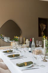 table préparée pour un dîner avec des bougies, bouteille de vin et des serviettes vertes roulées dans les assiettes blanches