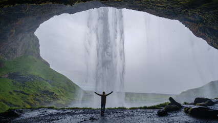 Seljalandsfoss waterfall cascades down from a rocky cliff, creating a breathtaking view from within...