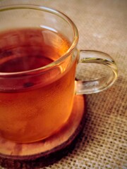 Steaming Herbal Tea in Clear Glass Mug on Rustic Coaster, Burlap Background