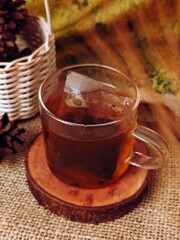 Warm Tea in Glass Cup with Pinecones on Burlap Background.