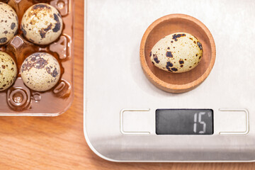 A speckled quail egg is weighed on a digital kitchen scale, displaying a weight of 15 grams beside...