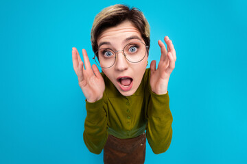Smiling young woman with short hair wearing glasses and a khaki shirt on a blue background...