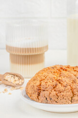 A freshly baked oatmeal cookie rests on a white plate beside a glass of layered coffee and...