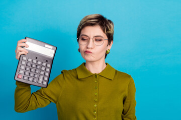 Casual woman holding calculator on blue background showing an expression of thoughtfulness in a...