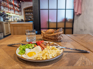 Hearty breakfast plate featuring scrambled eggs sunny-side-up egg sausage links roasted baby potatoes fresh greens and crusty bread basket