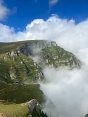 Clouds rolling over green mountain cliffs in a surreal alpine landscape