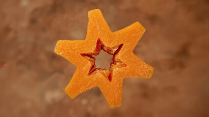 Star-shaped slice of ripe papaya fruit on a neutral background showcasing vibrant orange color and unique star configuration.