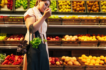Young woman holding a bag with vegetables in her bent hand, standing at shelves in a grocery store