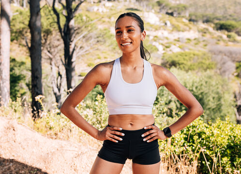 Young smiling female with hands on her hips, standing confidently ina  natural park during workout