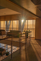 Golden sunlight streaming through sheer curtains casting soft shadows on modern lounge area with metal railing and plush seating