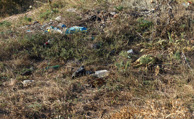 Littered area with plastic waste and debris among dry grass and shrubs