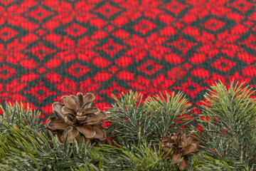 christmas background with fir branches and cones on knitted red and green fabric