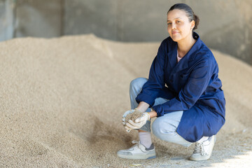 Asian woman farmer takes handful of granulated feed in palm of hand, checks purity and absence of...