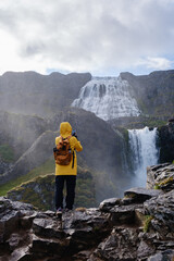 A traveler in a bright yellow rain jacket stands on rocky terrain, capturing the striking...