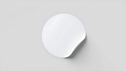 A minimalistic shot of a single white round sticker with a curled edge on a light gray background