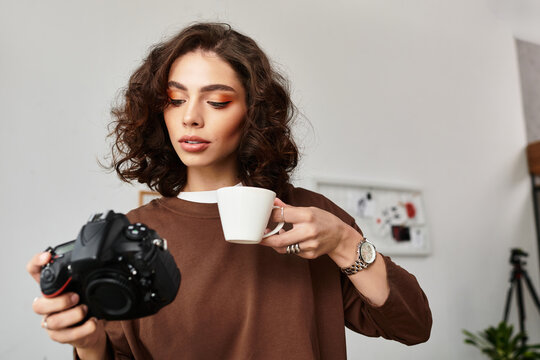 Young woman with curly hair enjoys coffee while reviewing her photography work at home